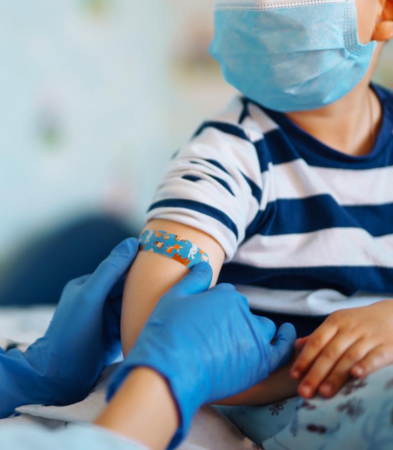 A nurse puts a bandaid on a childs arm after receiving a vaccination